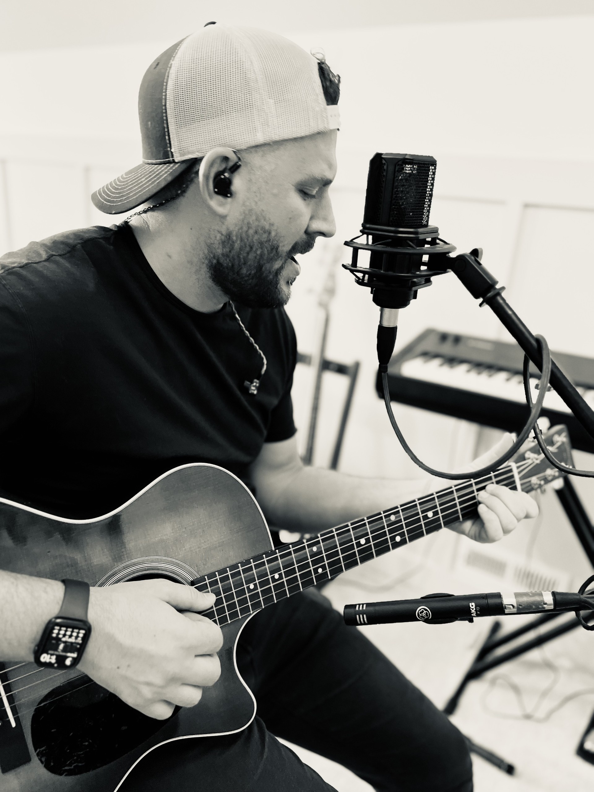 Riley Wilkinson singing into a studio microphone with an acoustic guitar